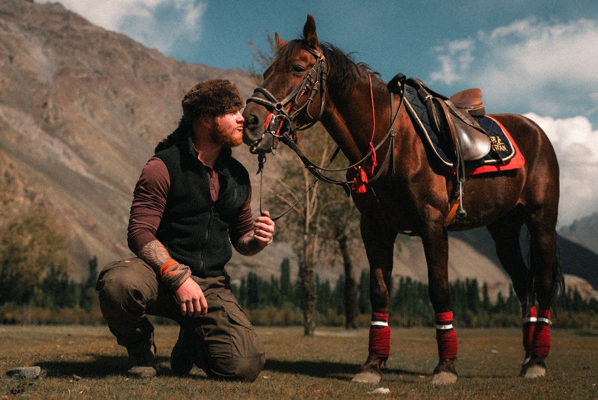 Charlie Maughan kneeling beside his bay horse in a mountain meadow