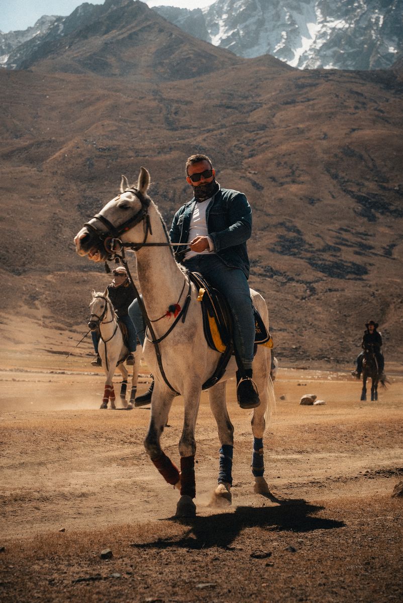 Sami Hermes riding a grey horse toward camera in an arid mountain valley